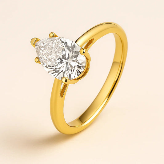 Gold plated ring with a pear-shaped diamond on a beige background