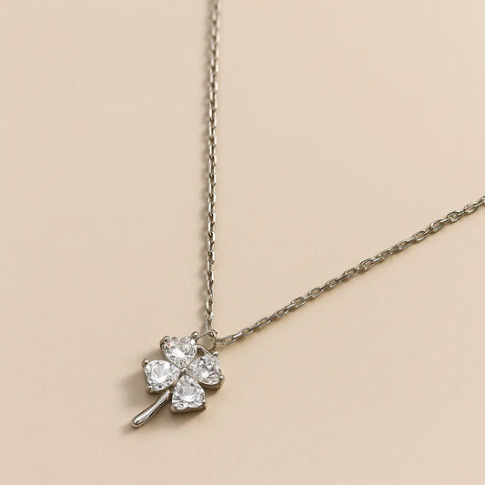 Silver necklace with a clover-shaped pendant on a beige background