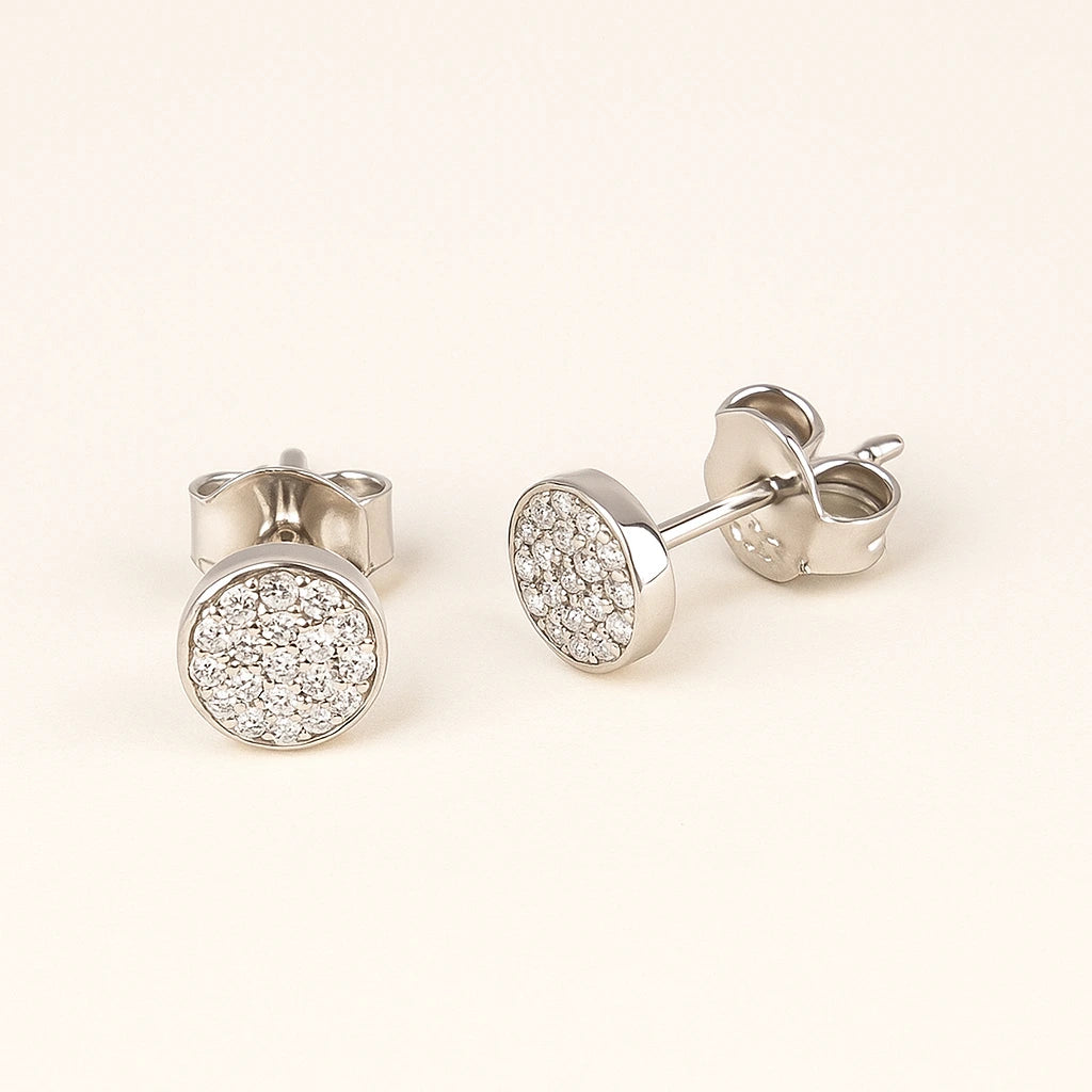 Silver stud earrings with clear gemstones on a light beige background