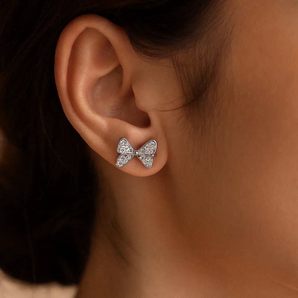 Silver bow-shaped earring worn on an ear with a blurred background