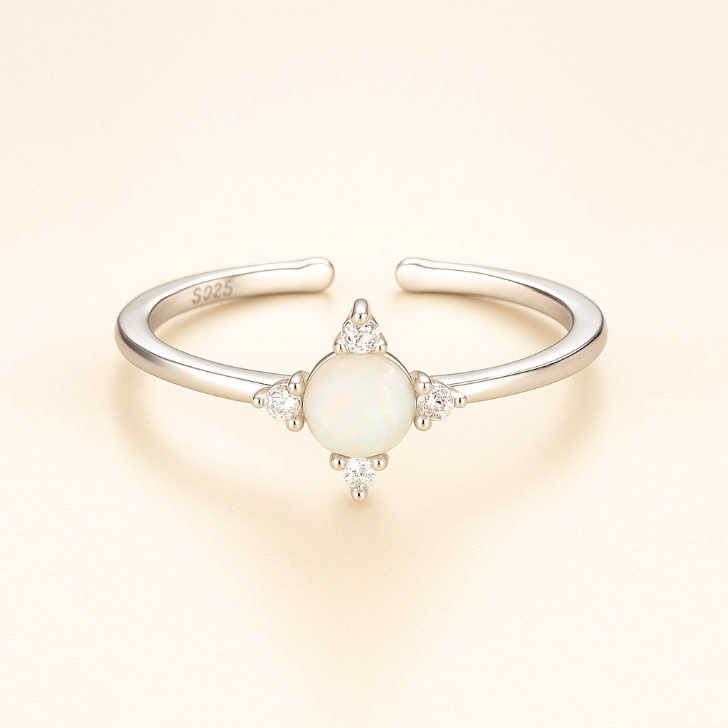 Silver ring with a central opal stone and smaller diamonds on a light beige background