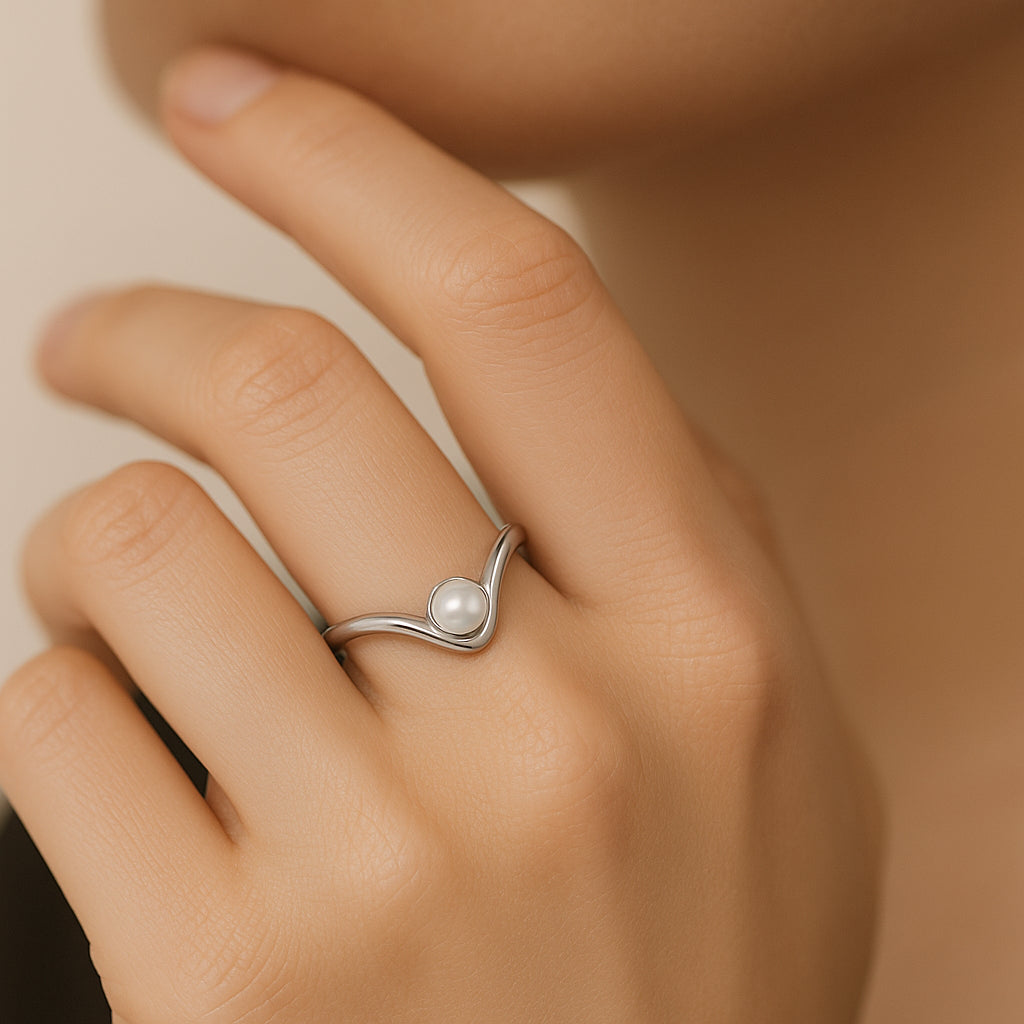 Silver ring with a pearl on a person's finger against a neutral background