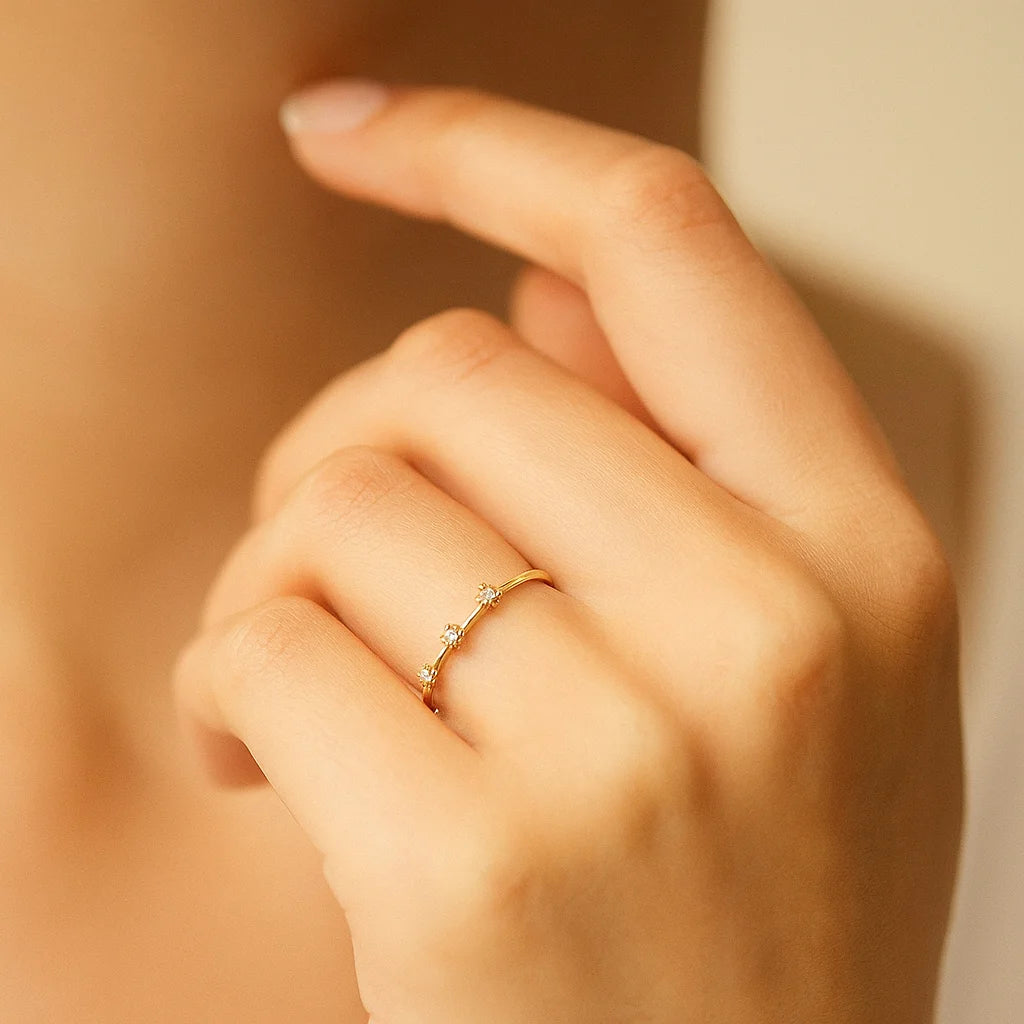 Close-up of a hand wearing a delicate golden ring with small diamonds on a warm-toned background.