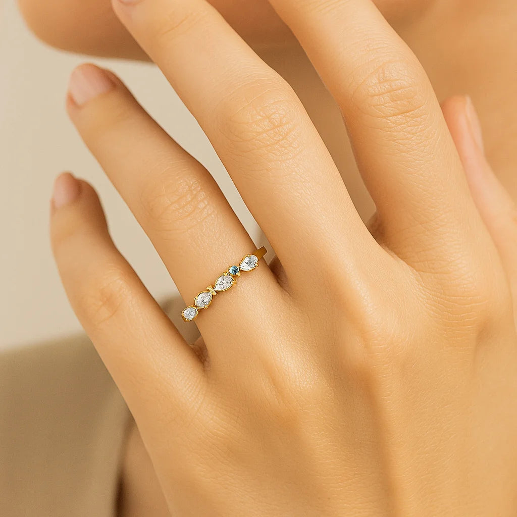 Hand wearing a golden ring with gemstones on a neutral background