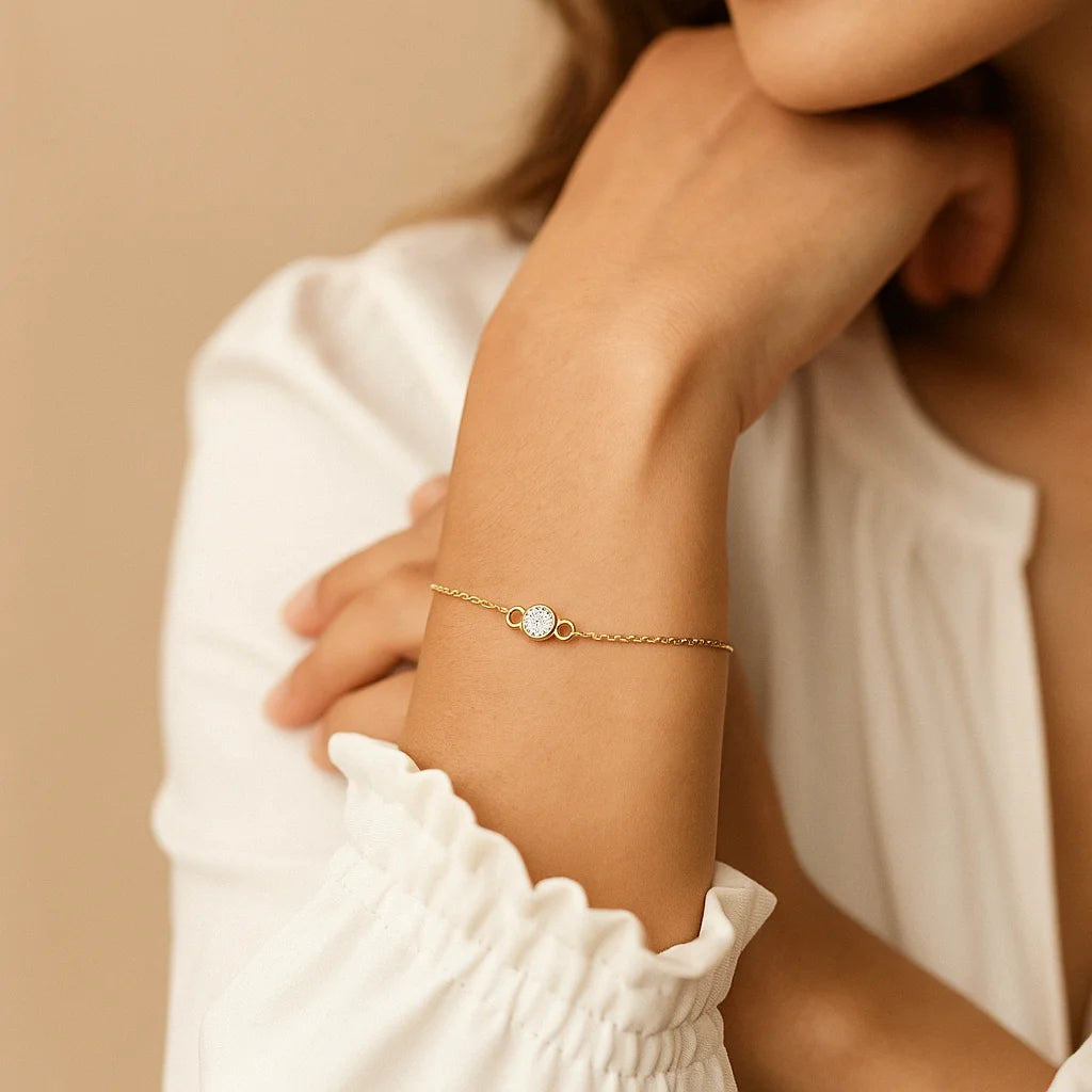 Golden bracelet with a heart-shaped gemstone on a person's wrist against a beige background