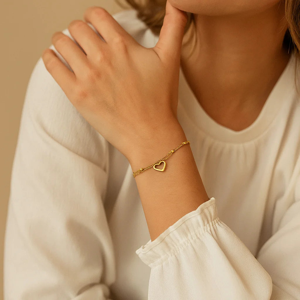 Close-up of a person wearing a gold bracelet with a heart charm on a beige background