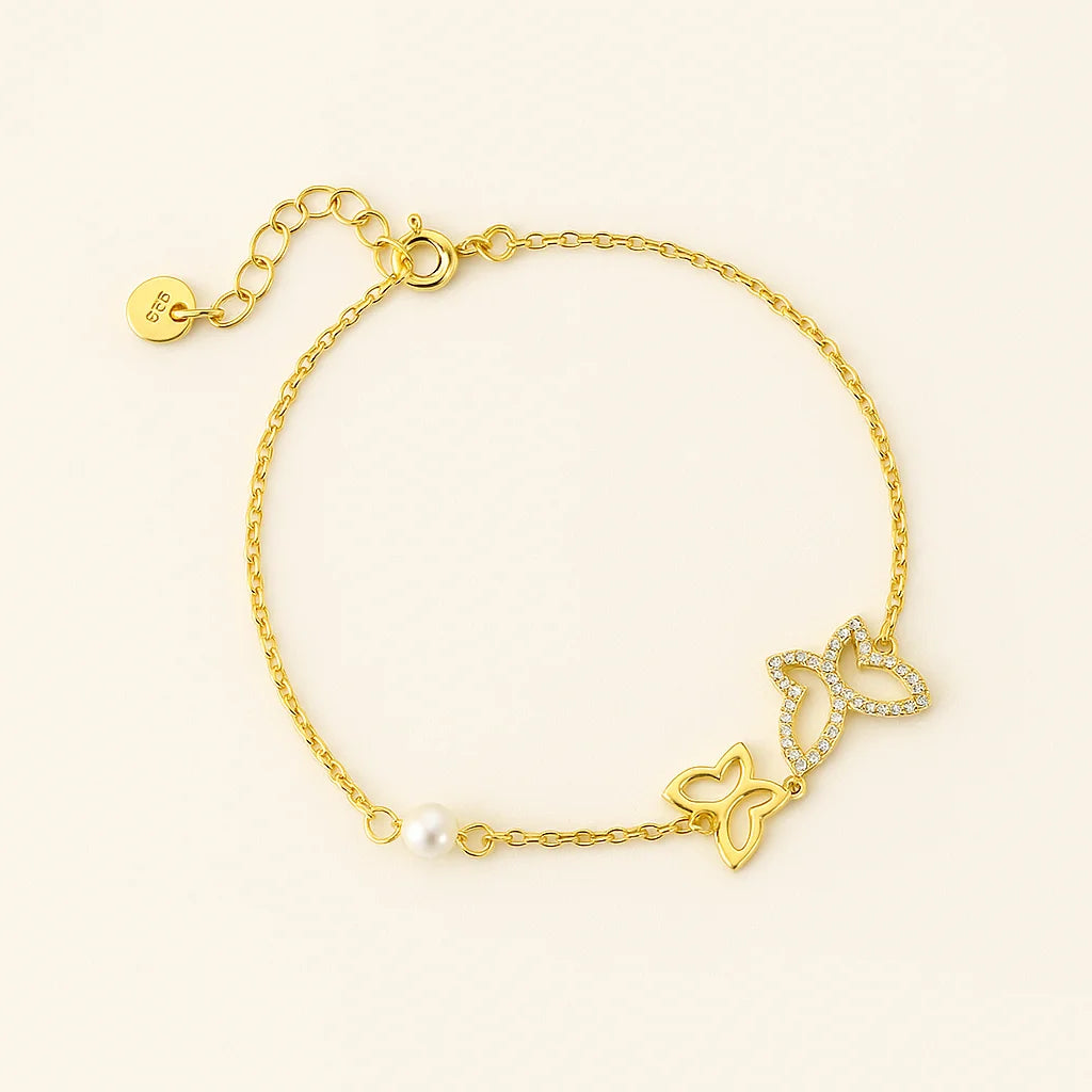 Gold bracelet with butterfly charms and a pearl on a light beige background
