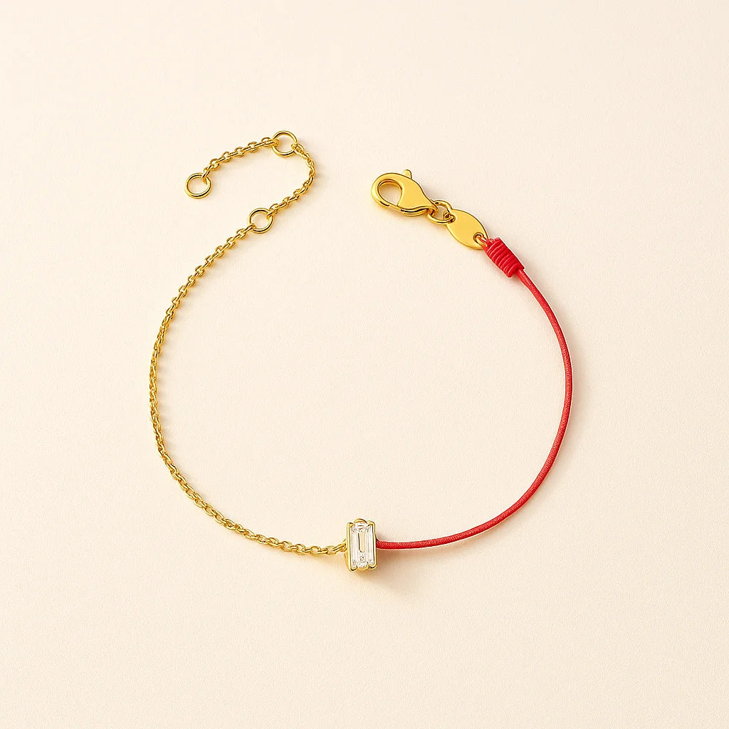 Gold bracelet with a red string and clear gemstone on a beige background