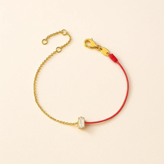 Gold bracelet with a red string and clear gemstone on a beige background