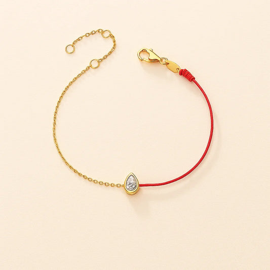 Gold bracelet with a teardrop-shaped charm on a beige background