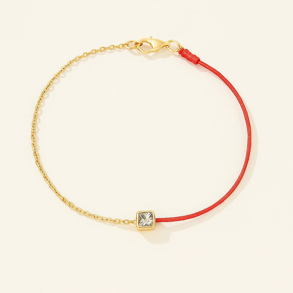 Bracelet with red cord and gold clasp on a beige background