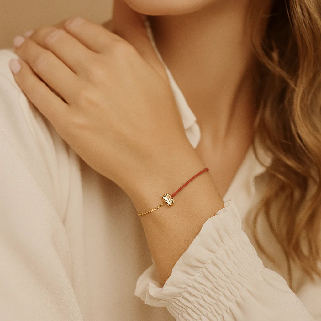 Close-up of a person wearing a delicate bracelet with a small square charm on a neutral background