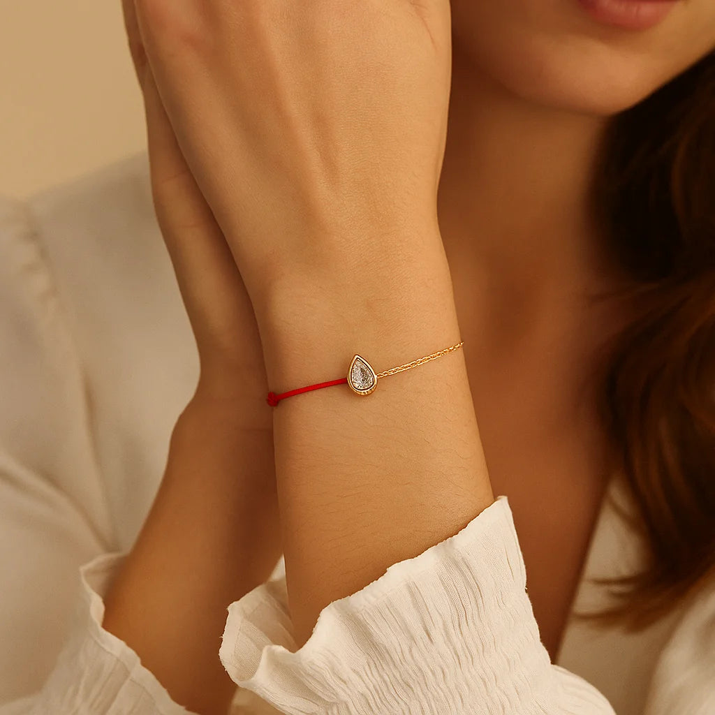 Close-up of a person wearing a gold bracelet with a red string on a beige background