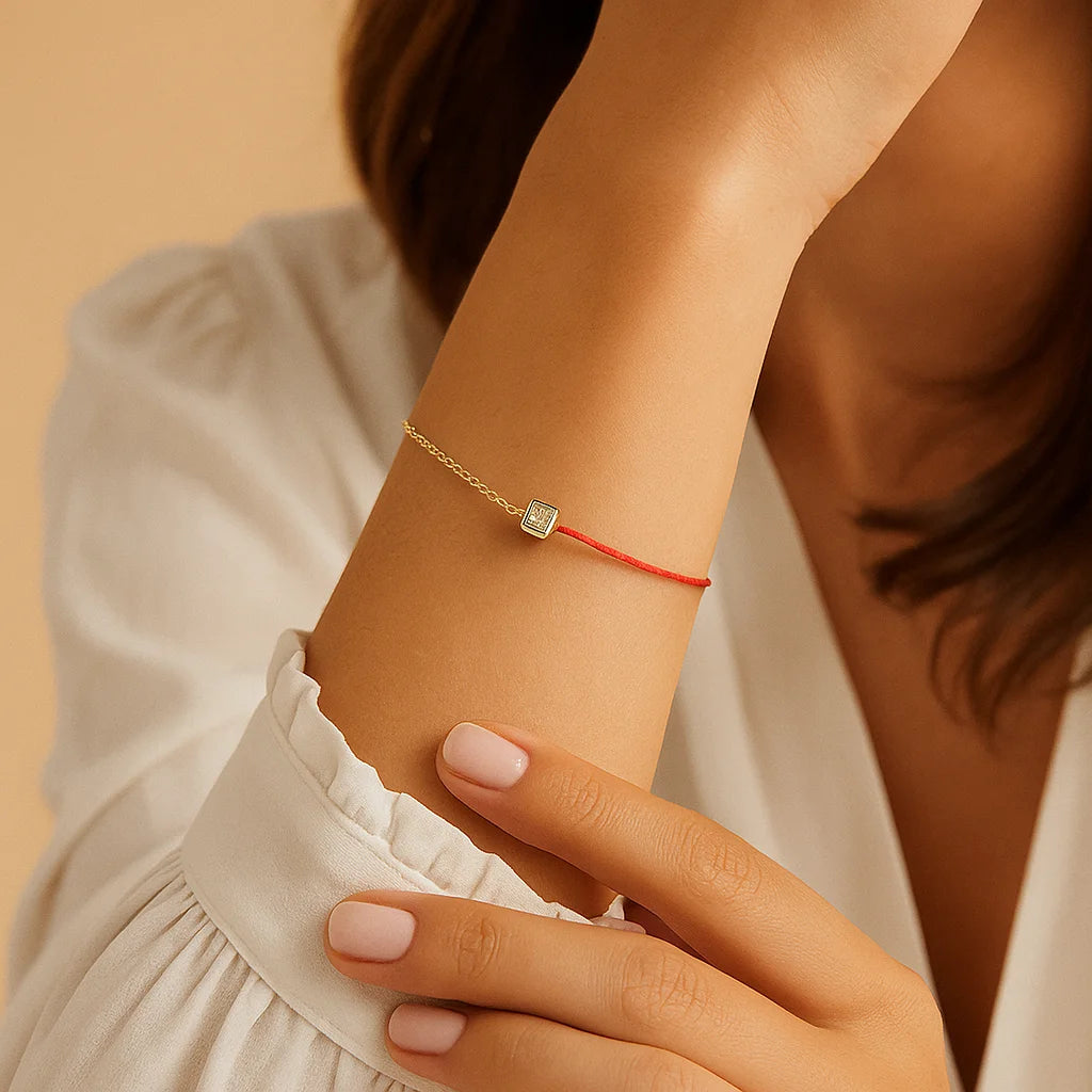 Close-up of a wrist wearing a red bracelet with a gold clasp on a beige background