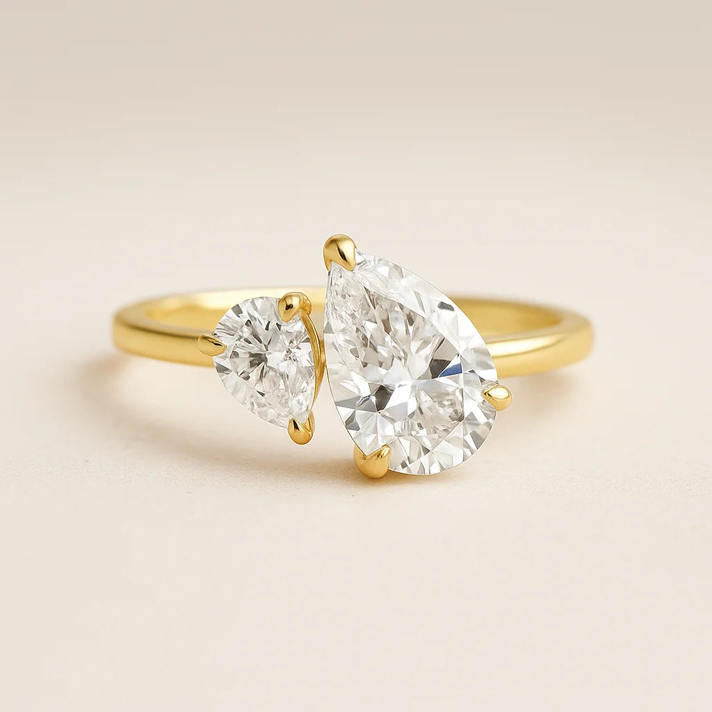 Gold ring with two pear-shaped diamonds on a beige background