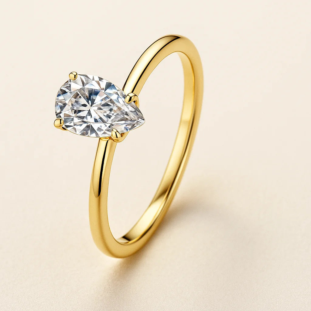 Gold ring with a pear-shaped diamond on a beige background