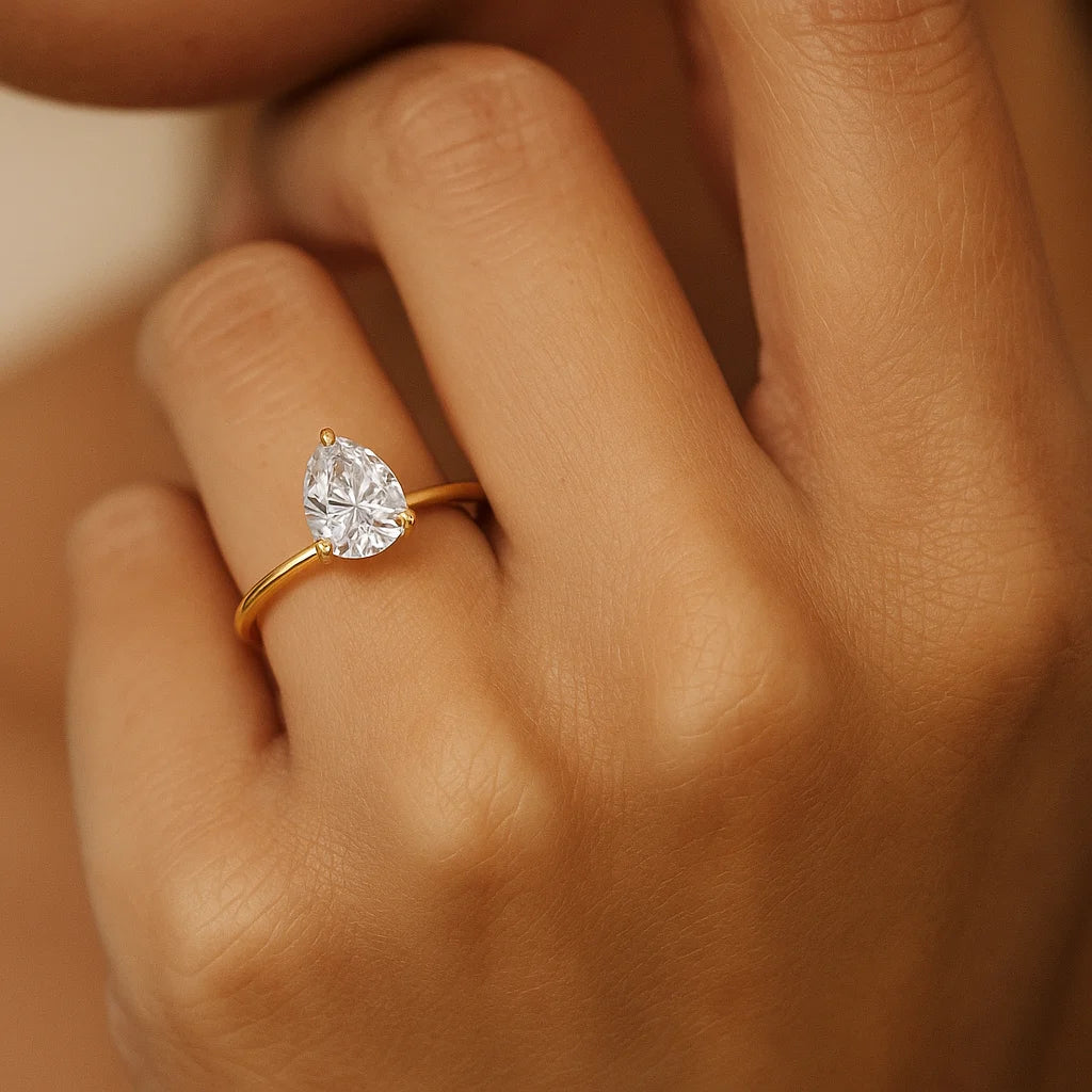 Gold ring with a pear-shaped diamond on a hand against a neutral background