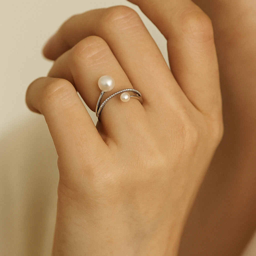 Hand wearing a silver ring with pearls against a neutral background