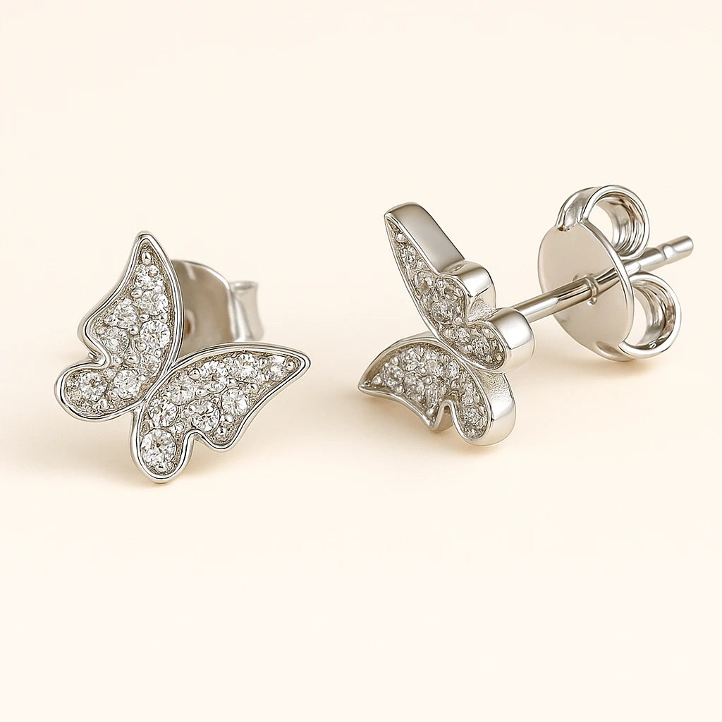 Butterfly-shaped silver earrings with clear gemstones on a light beige background