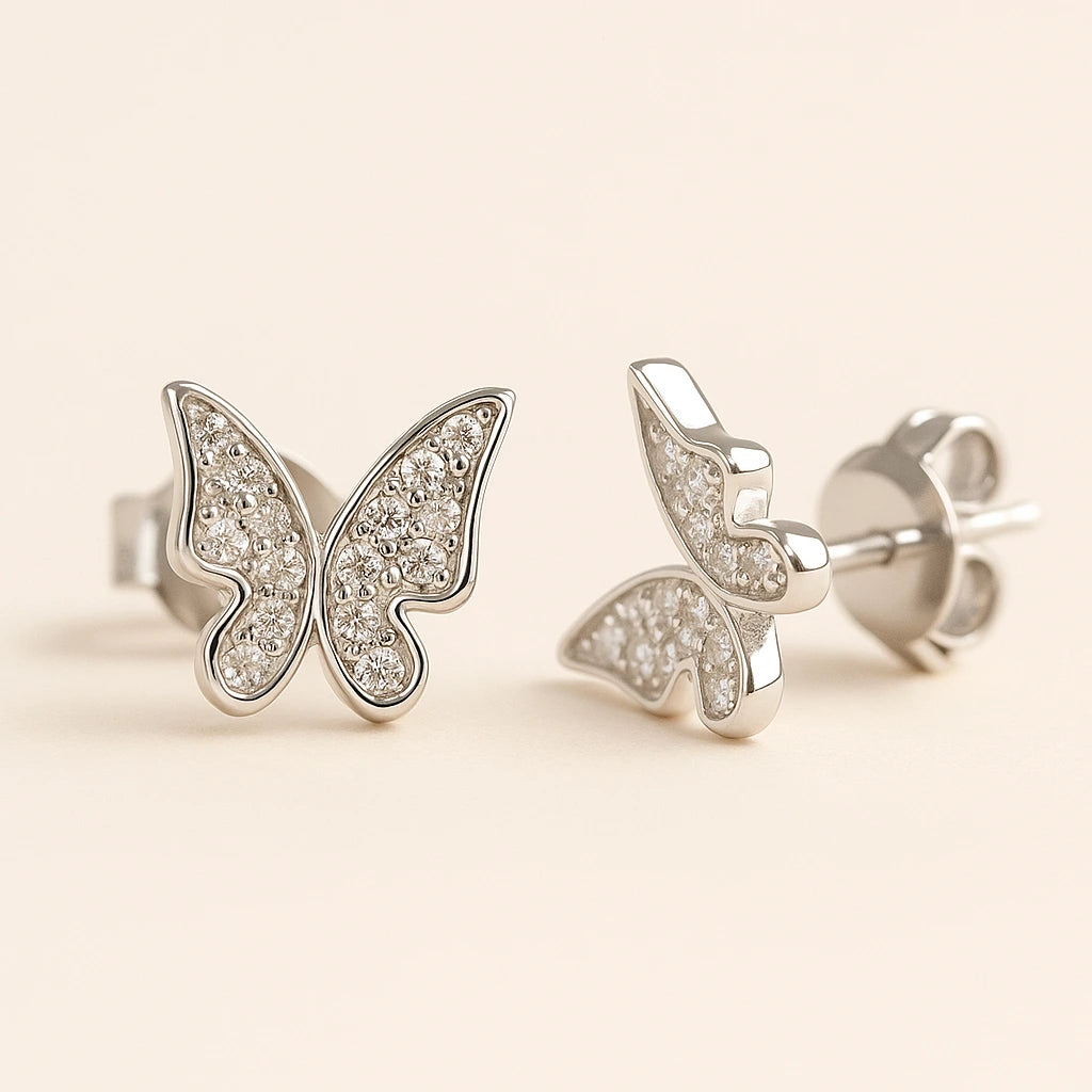 Butterfly-shaped silver earrings with gemstones on a beige background