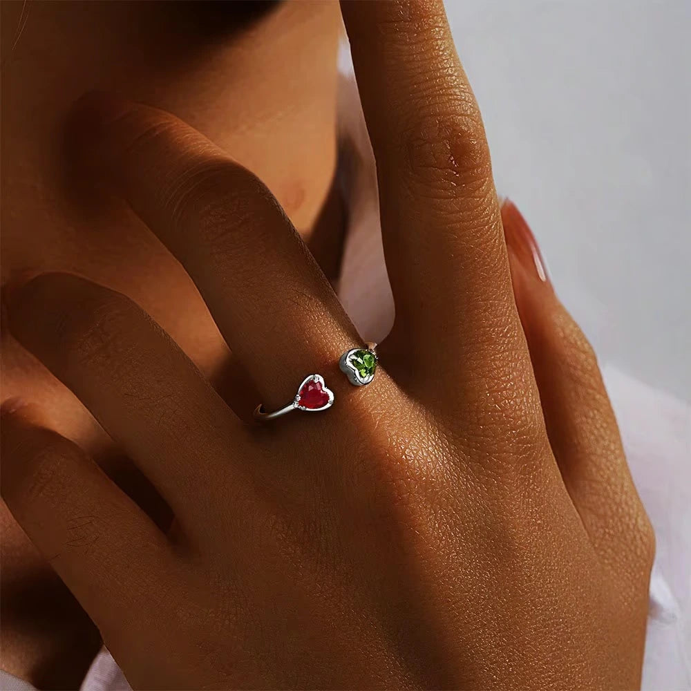 Close-up of a hand wearing two small heart-shaped rings with colorful stones.
