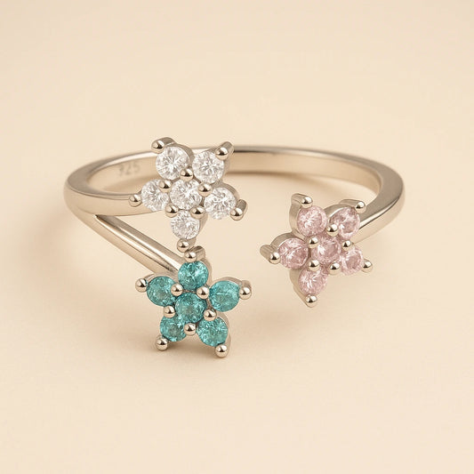 three floral-shaped rings with gemstones on a beige background