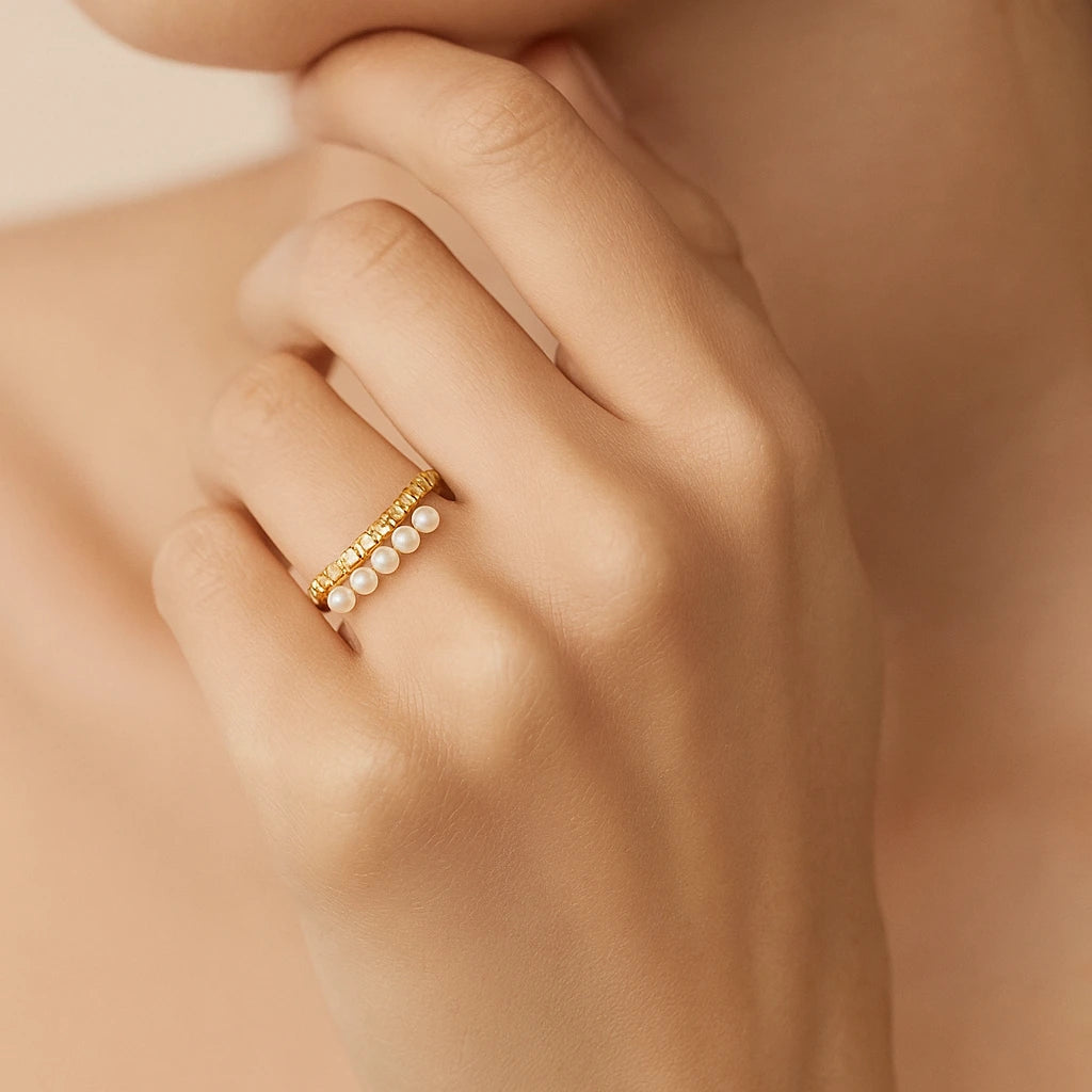 Golden ring with pearls on a hand against a neutral background