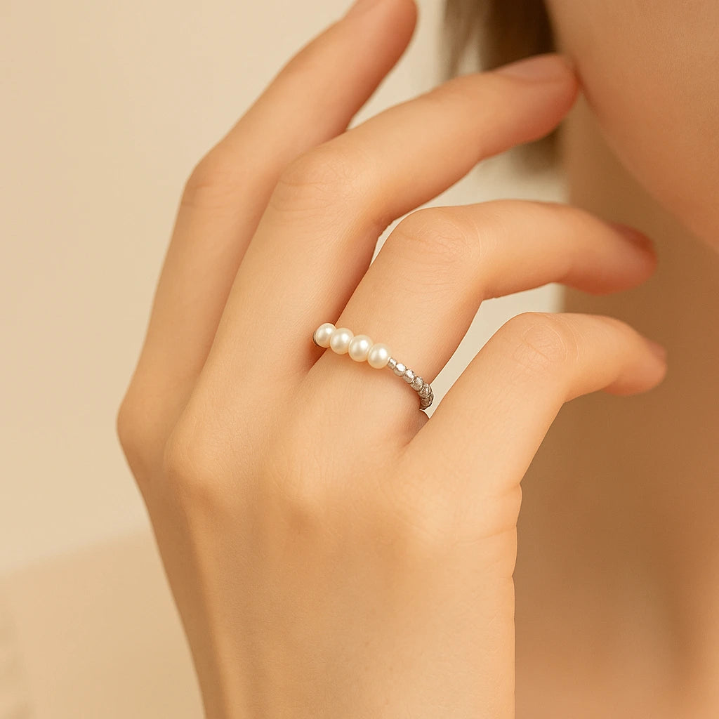 Hand wearing a pearl ring on a neutral background