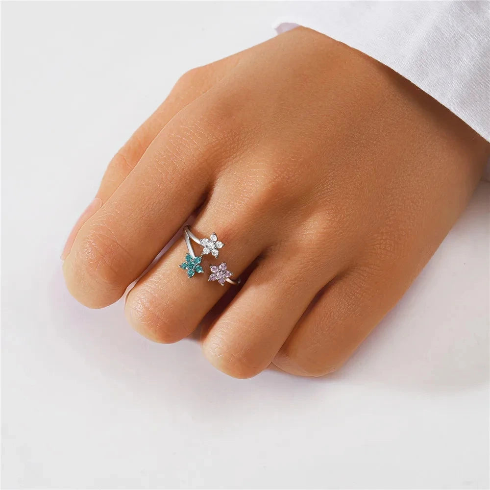 Hand wearing a silver ring with floral designs and gemstones on a white background