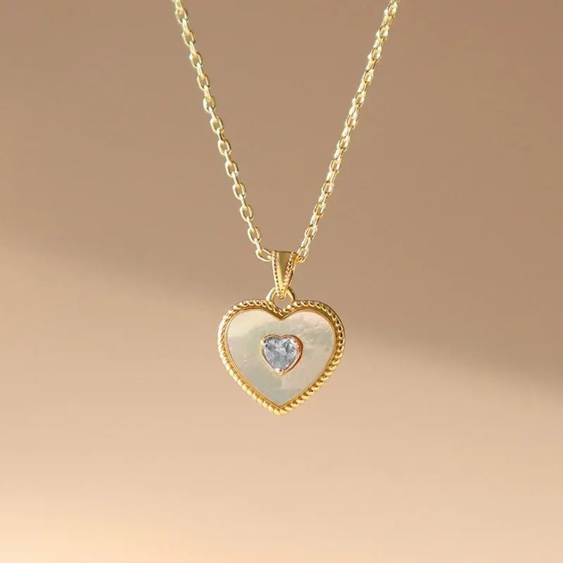 Gold heart-shaped necklace with a clear gemstone on a beige background