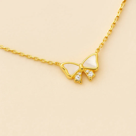 A charming gold-plated sterling silver necklace featuring a bow-shaped pendant with mother-of-pearl and cubic zirconia details.
