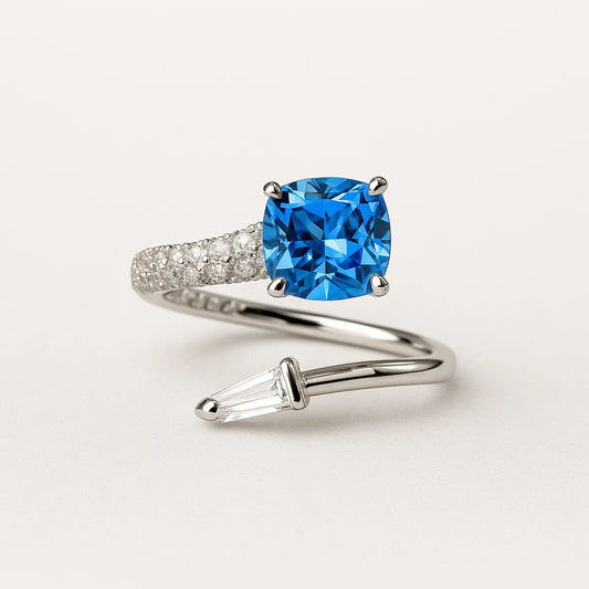 A 925 sterling silver open-band ring with a blue square-cut stone, a baguette stone, and pavé cubic zirconia.