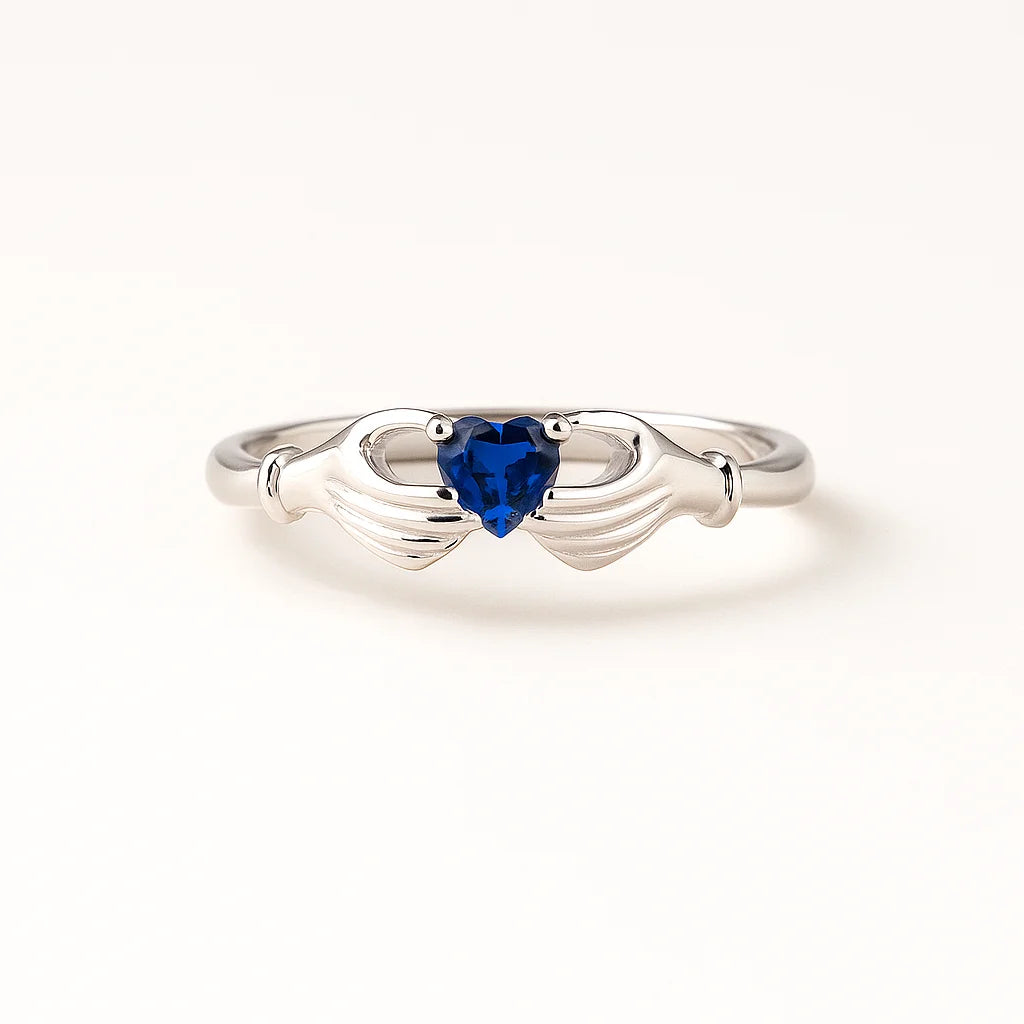 A 925 sterling silver ring with a central heart-shaped blue stone held by two hands.