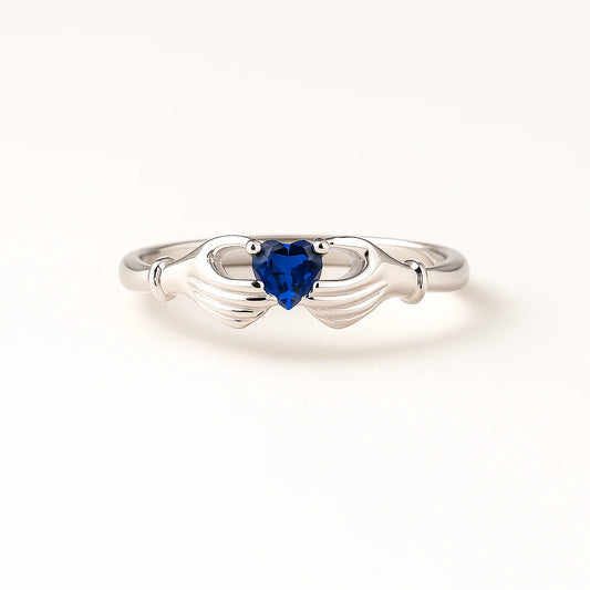 A 925 sterling silver ring with a central heart-shaped blue stone held by two hands.