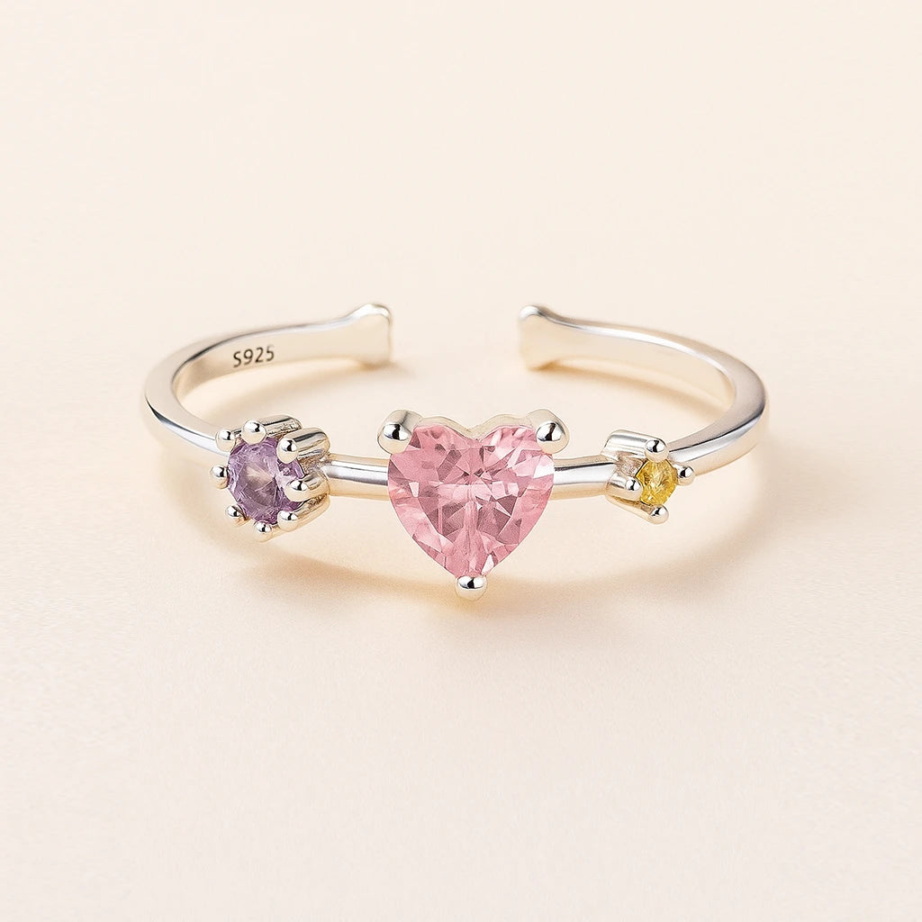 Three-stone ring with heart-shaped pink gemstone on a beige background