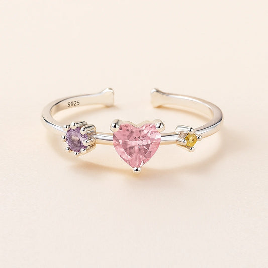 Three-stone ring with heart-shaped pink gemstone on a beige background